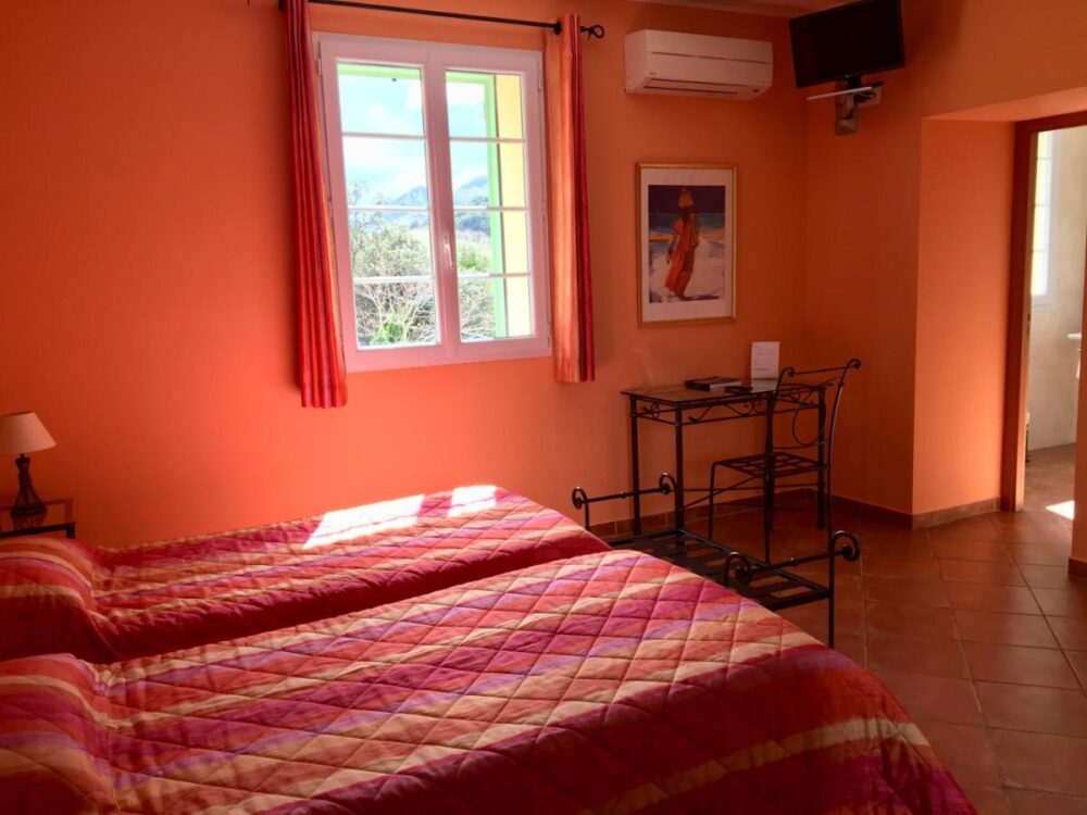 Chambre double avec murs orange et fenêtre.