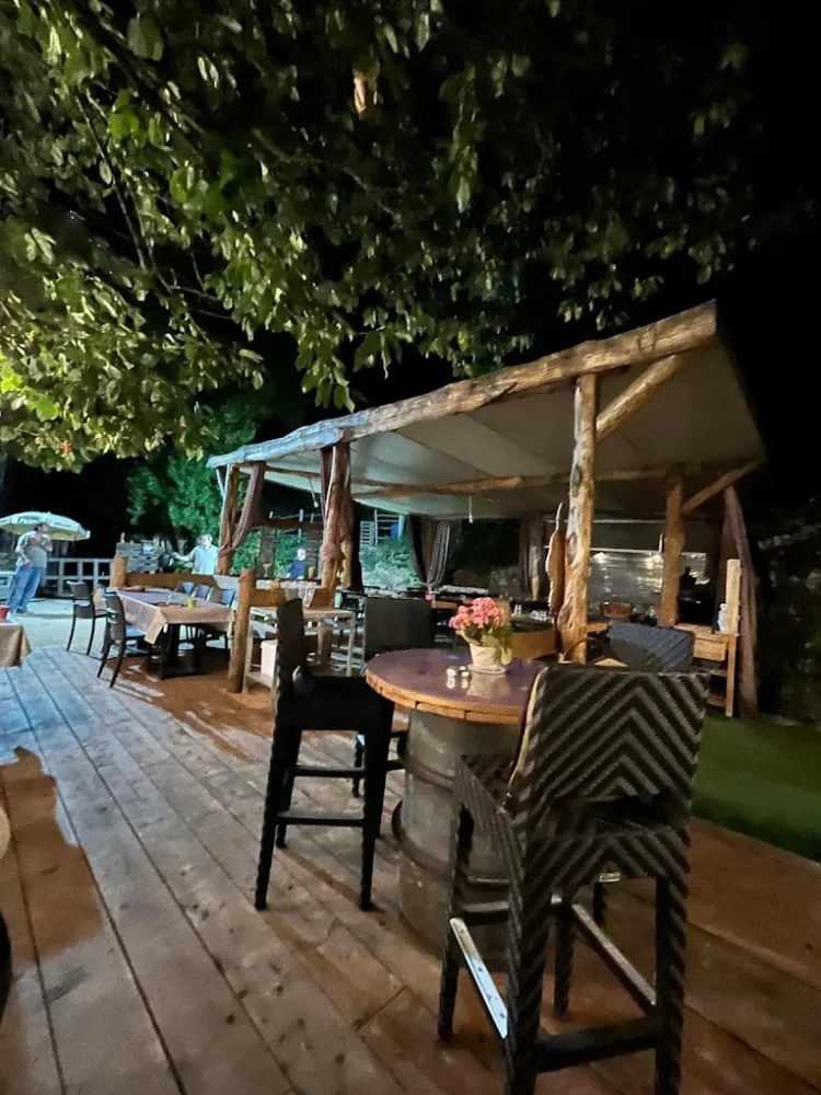 Terrasse en bois éclairée, tables et chaises le soir.