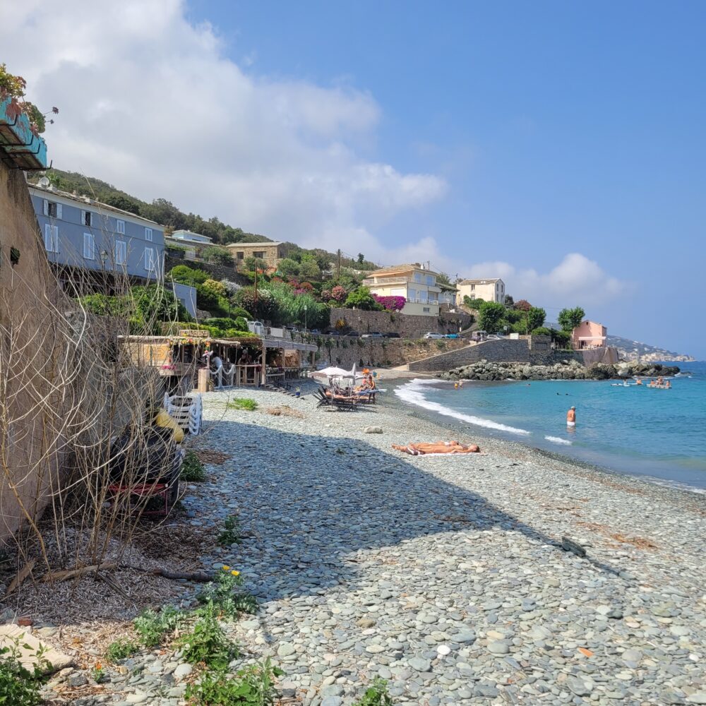 Plage de galets avec maisons en bord de mer.