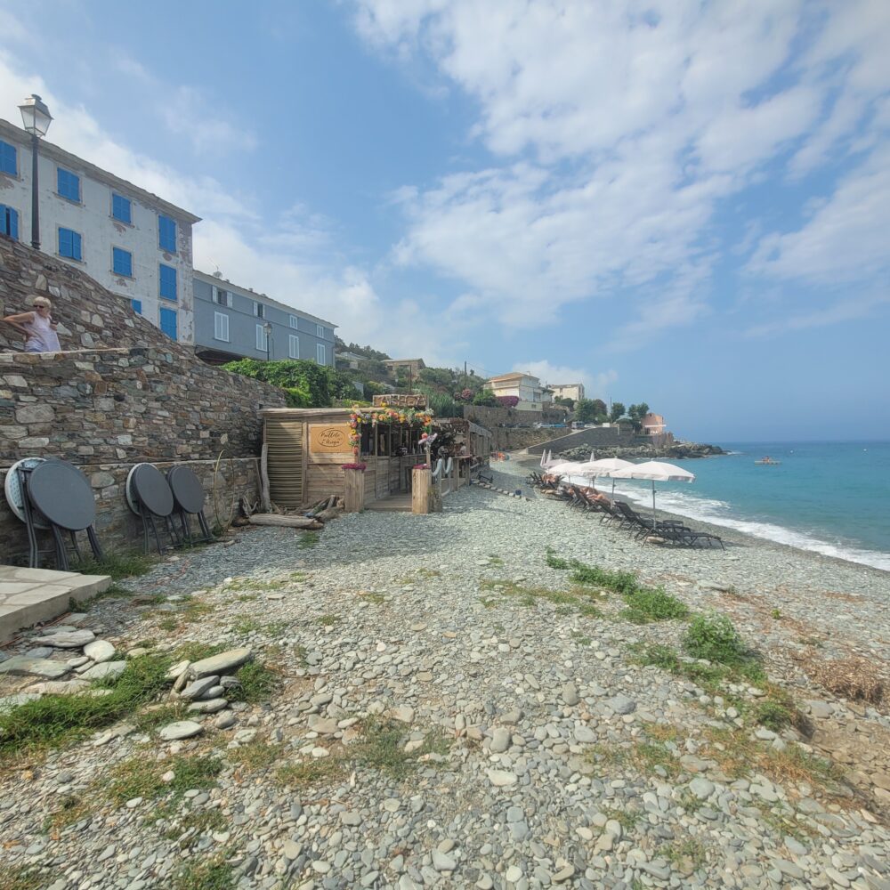 Plage caillouteuse avec restaurant et transats.