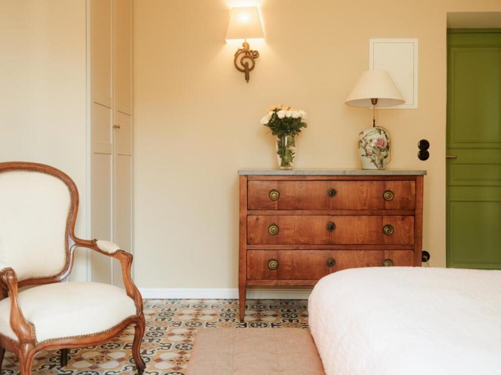 Chambre avec fauteuil, commode, et lampe.