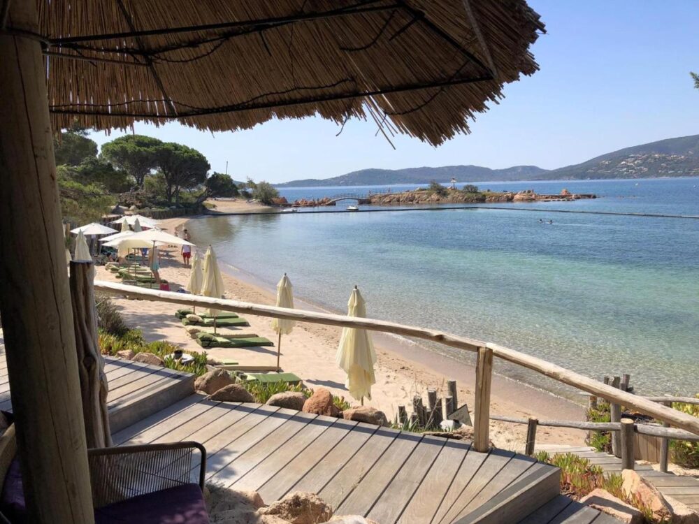 Plage avec parasols, vue sur mer et montagnes.
