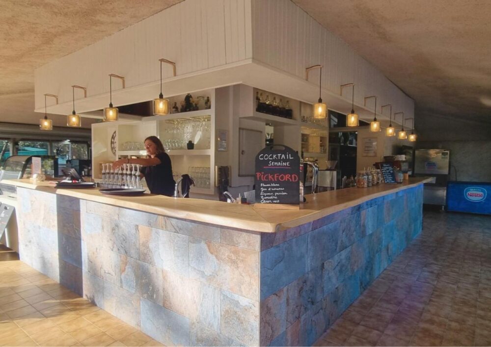 Bar en pierre avec barman et menu de cocktails.