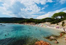 Plage méditerranéenne bondée, parasols colorés, mer turquoise.