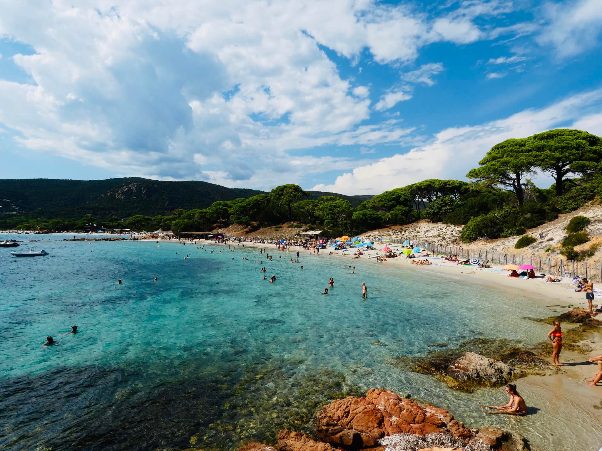 Plage méditerranéenne bondée, parasols colorés, mer turquoise.