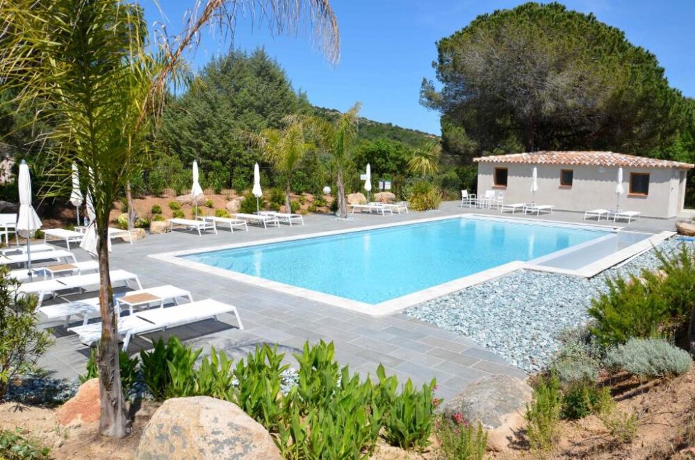 Piscine extérieure entourée de chaises longues et arbres.