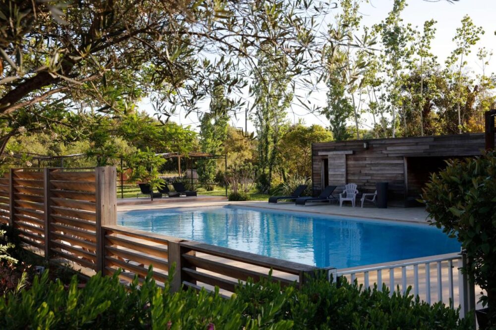 Piscine extérieure entourée de verdure et terrasse en bois.