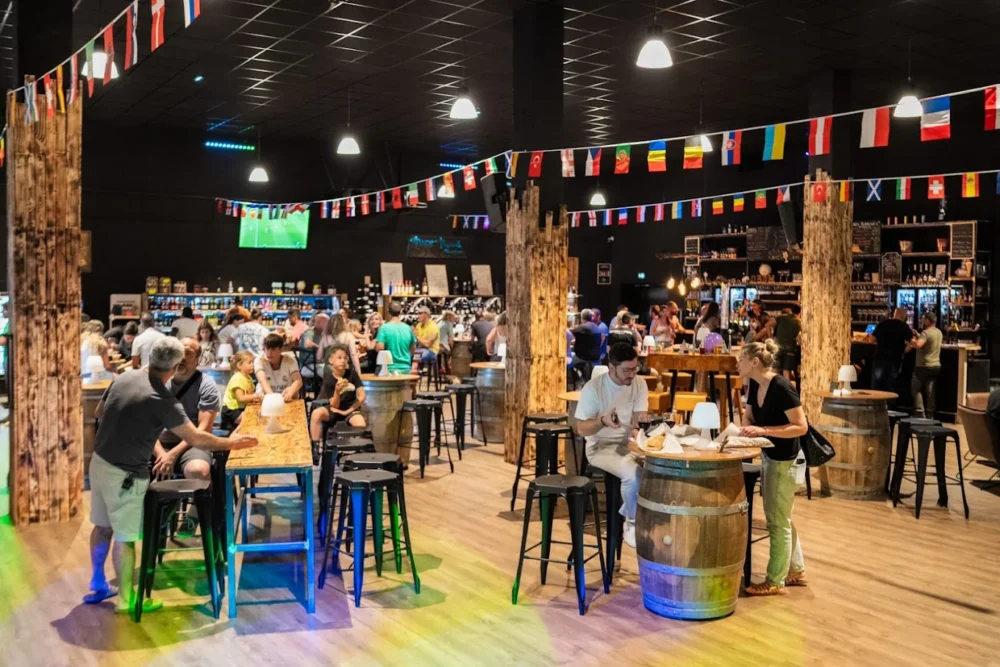 Personnes dans un bar animé avec drapeaux et tonneaux.