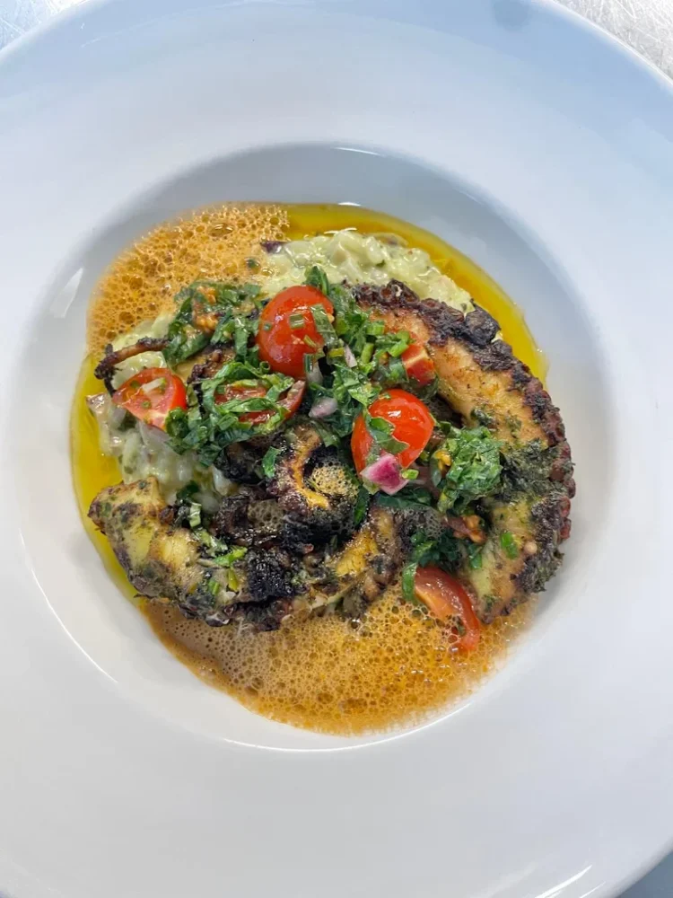 Plat de poulpe grillé avec légumes et sauce.