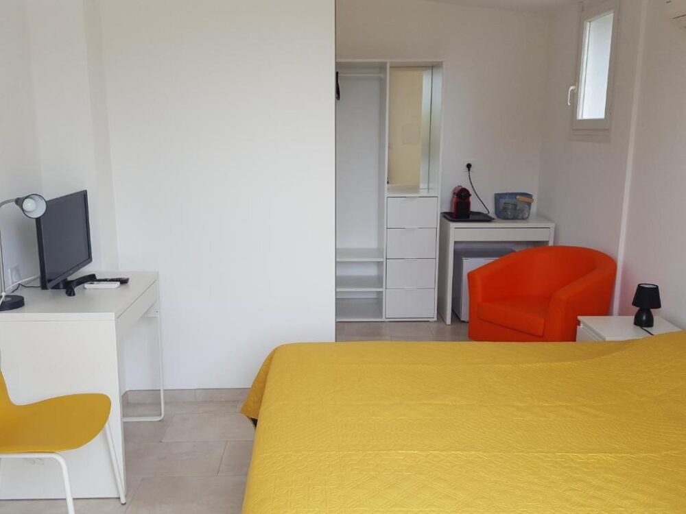 Chambre lumineuse avec chaise orange et lit jaune.