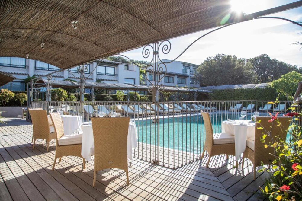Terrasse ensoleillée près d'une piscine avec tables.