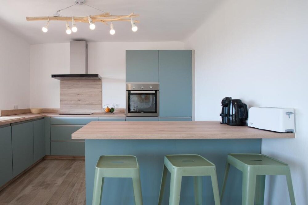 Cuisine moderne avec îlot central et tabourets verts.