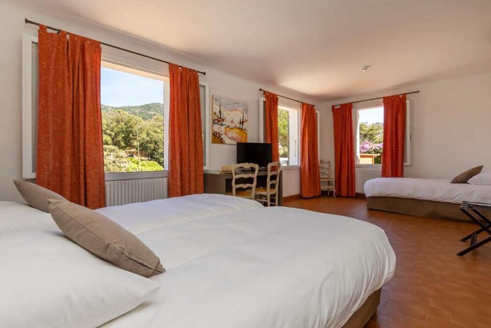 Chambre spacieuse avec trois lits et fenêtres ouvertes.
