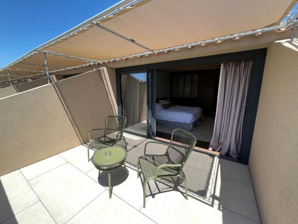 Terrasse ensoleillée avec trois chaises et table.