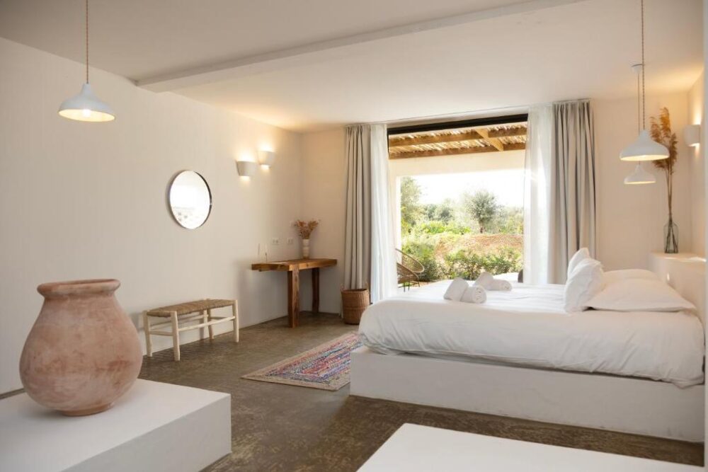 Chambre avec lit, grande fenêtre et poterie.