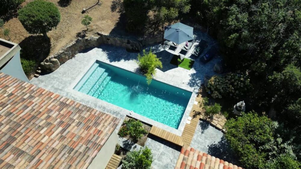 Piscine extérieure entourée de verdure et terrasse.