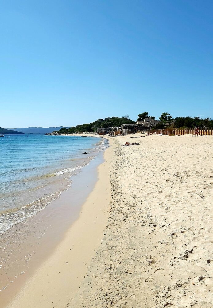 Plage ensoleillée avec mer bleue et sable clair.