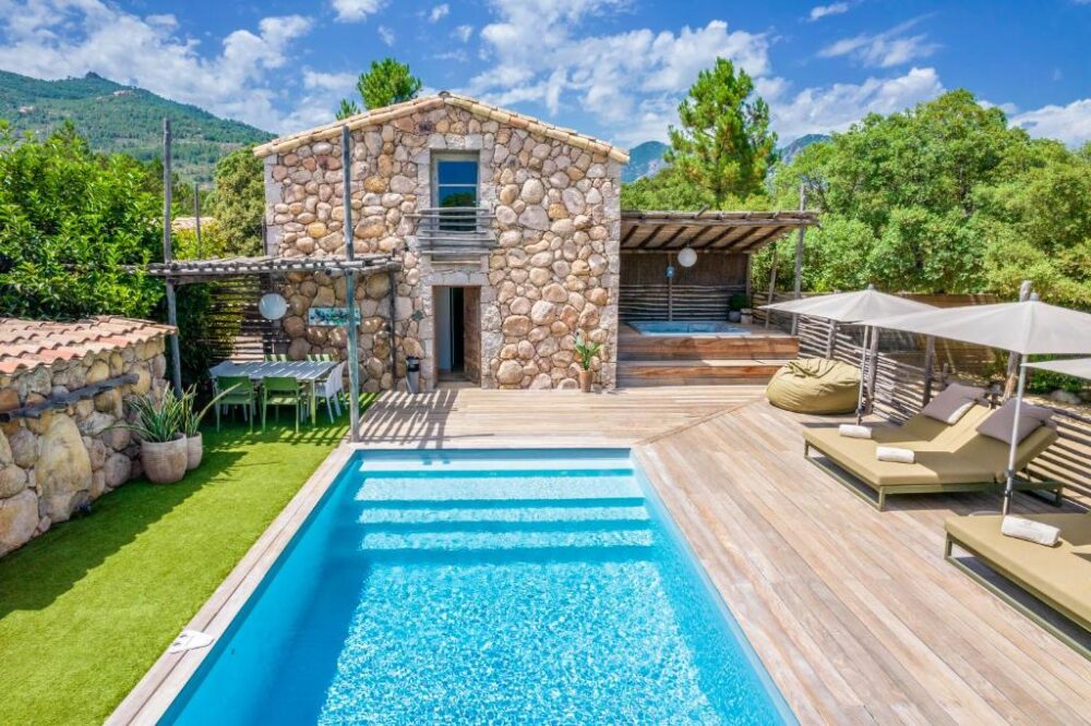 Maison en pierre avec piscine et terrasse en bois.