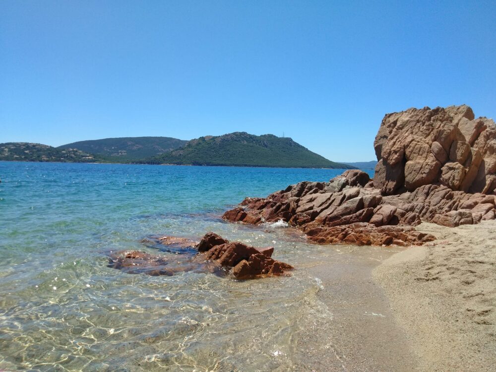 Plage rochers mer bleue montagne en arrière-plan.
