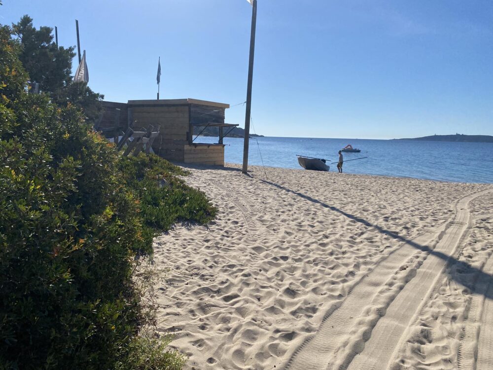 Plage ensoleillée avec cabane et bateau.