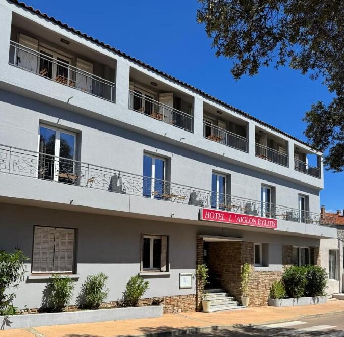 Façade de l'hôtel avec balcon et enseigne rouge.