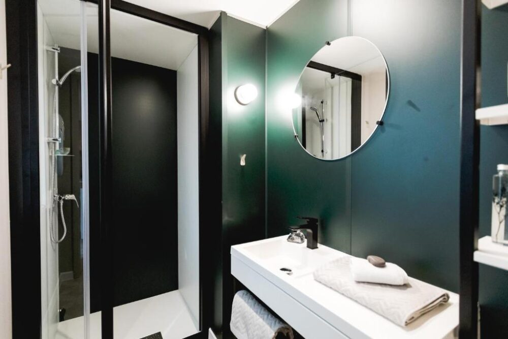 Salle de bain moderne avec douche et miroir rond.