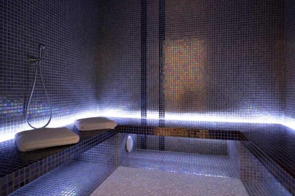 Hammam carreaux bleus avec lumière douce, serviettes sur banc.