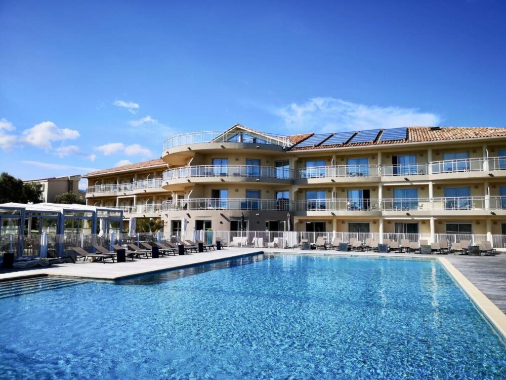 Hôtel moderne avec piscine et chaises longues ensoleillées.