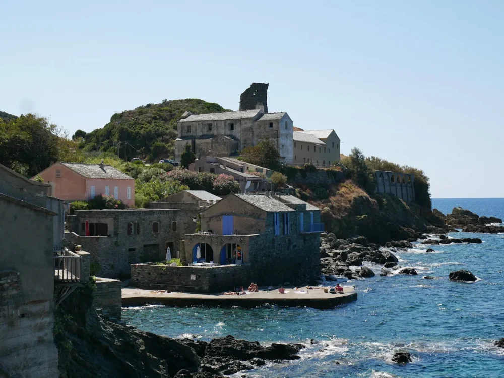 Village côtier méditerranéen avec maisons en pierre, mer bleue.