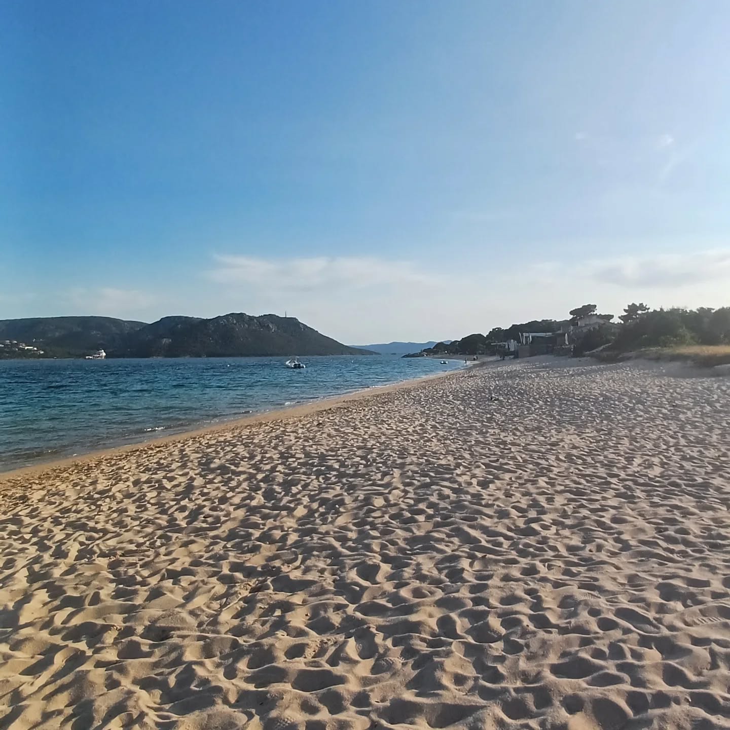 Plage sableuse avec mer et montagnes.