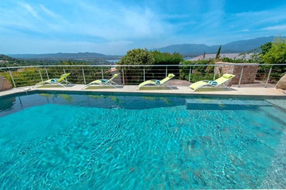 Piscine avec vue sur montagnes et transats verts.