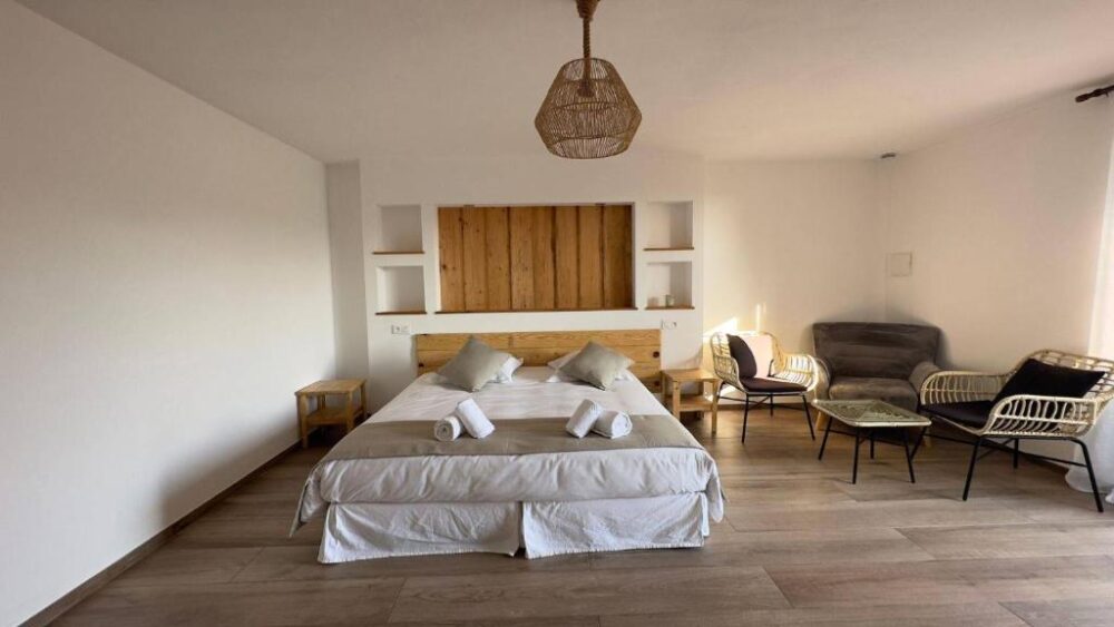Chambre lumineuse avec lit double et fauteuils.