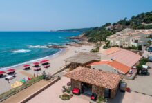 Plage méditerranéenne avec parasols rouges et villas.