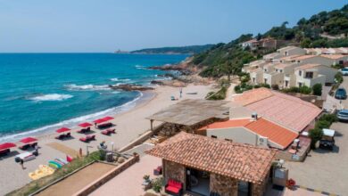 Plage méditerranéenne avec parasols rouges et villas.