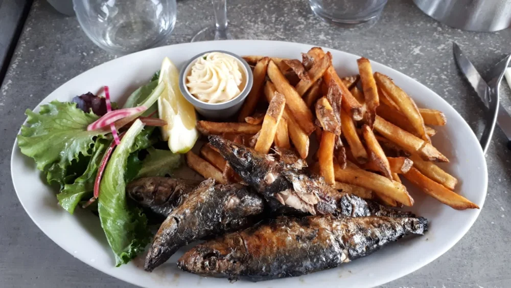 Assiette de sardines grillées avec frites et salade.