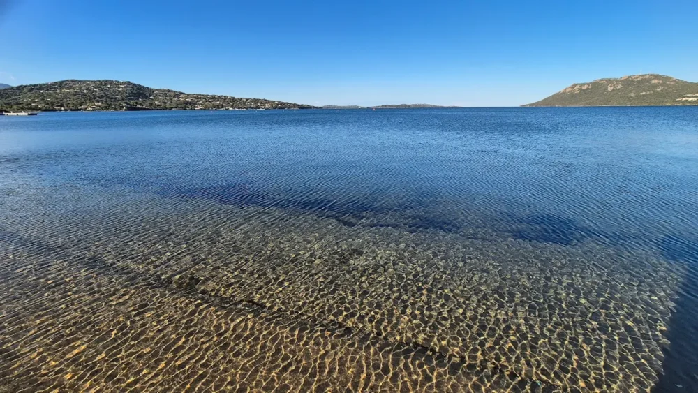 Plage avec eau claire et montagnes lointaines.
