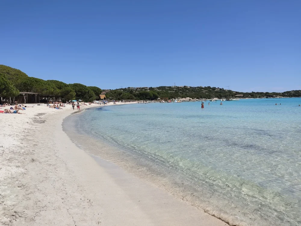 Plage de sable avec eaux cristallines et baigneurs.