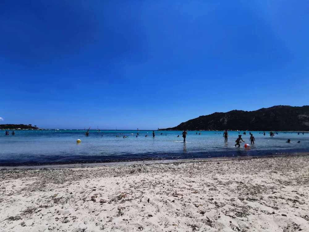 Plage ensoleillée avec baigneurs et montagnes en arrière-plan.