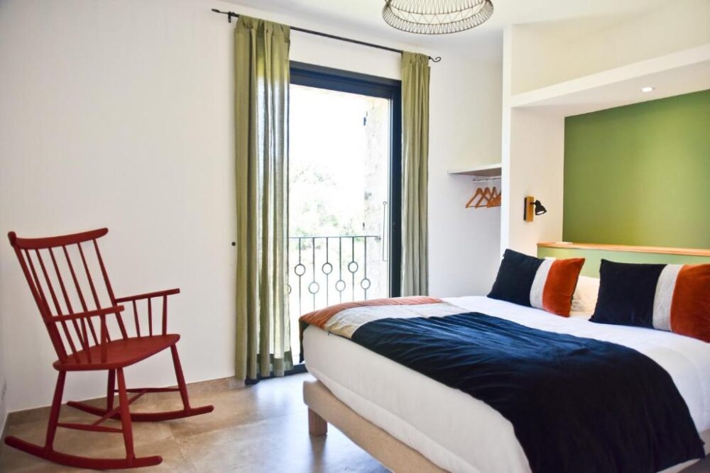 Chambre lumineuse avec lit et fauteuil rouge.