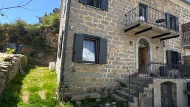 Maison en pierre avec balcons et jardin verdoyant.